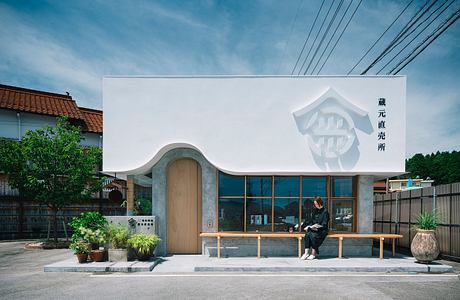 A modern, minimalist-style Japanese building with an arched entrance and large windows overlooking a courtyard.