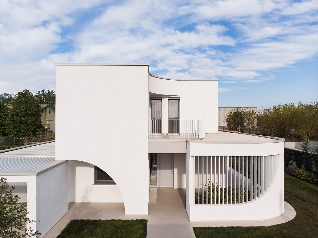 Modern, white, curved exterior with balcony and large windows overlooking lush greenery.