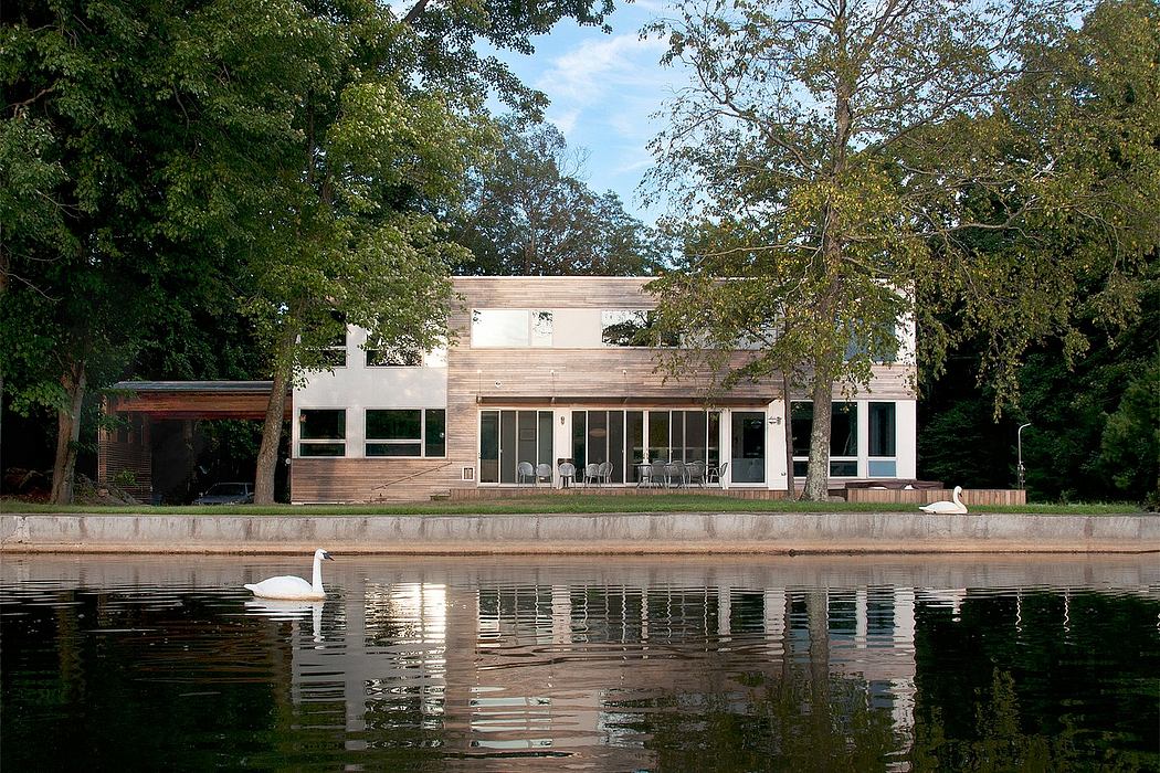 A modern, wooden lakefront home with large windows and a serene pool reflection.