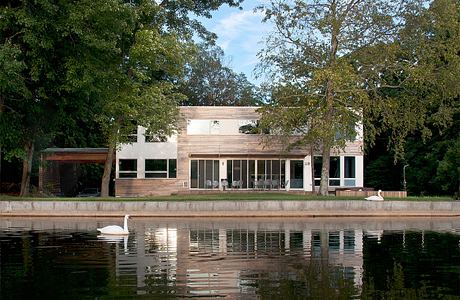 A modern, wooden lakefront home with large windows and a serene pool reflection.