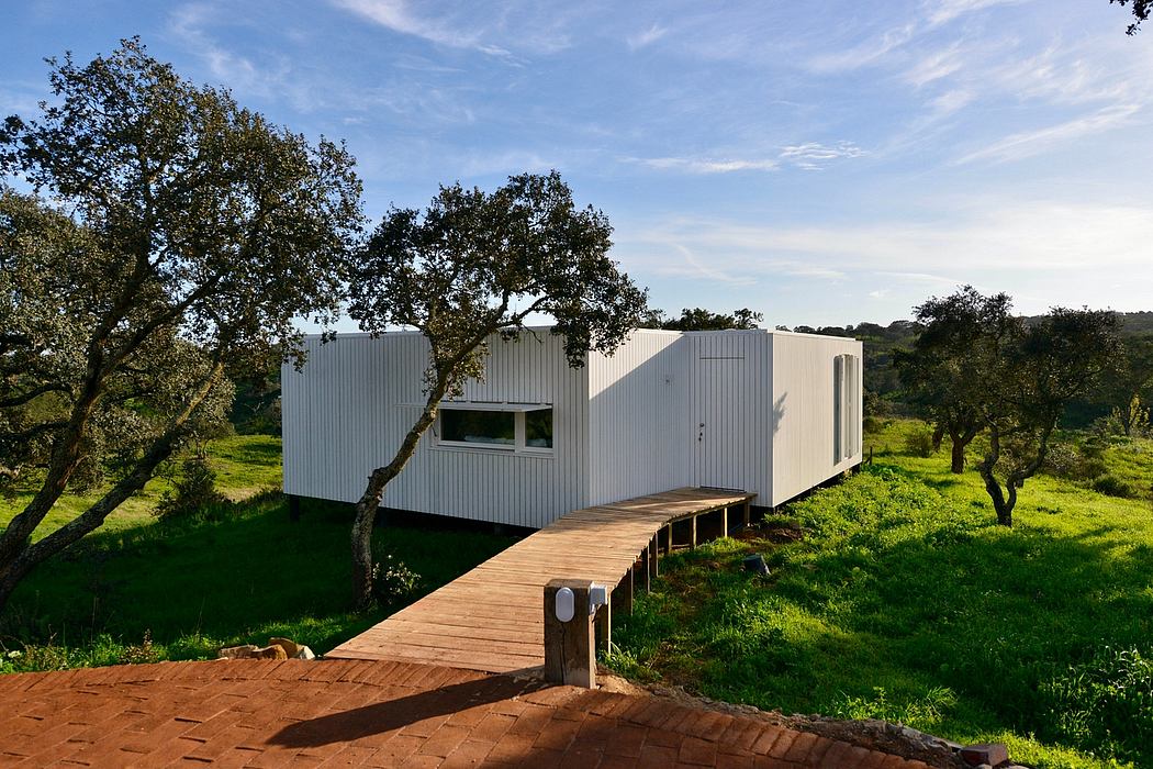 Modern, white-walled cabin nestled among lush trees; wooden walkway leads to entrance.