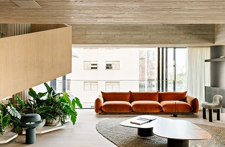 Warm, modern living space with rustic wood panels, plush orange sofa, and circular coffee tables.