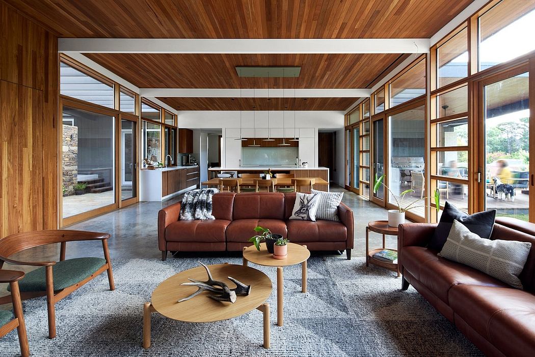 A modern, open-concept living space with wood-paneled ceilings, large windows, and plush leather sofas.