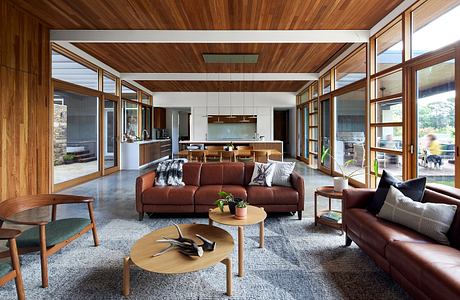 A modern, open-concept living space with wood-paneled ceilings, large windows, and plush leather sofas.