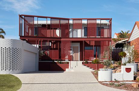 A striking two-story home with a distinctive red steel frame, brick walls, and expansive windows.