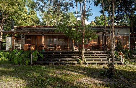 A rustic wooden cabin nestled among lush greenery, with a covered porch and wooden steps leading up.