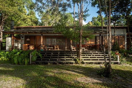 A rustic wooden cabin nestled among lush greenery, with a covered porch and wooden steps leading up.