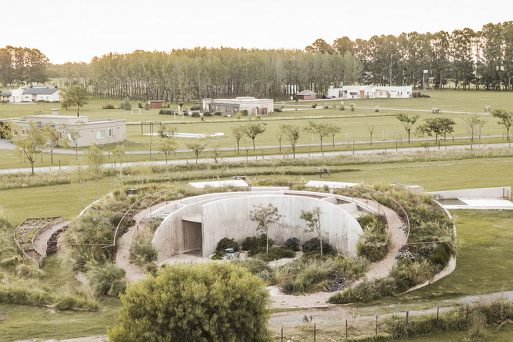 Circular concrete structure with integrated landscaping in grassy field surrounded by trees.