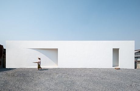 Clean, minimalist architecture with stark white walls, open spaces, and a person standing in the foreground.