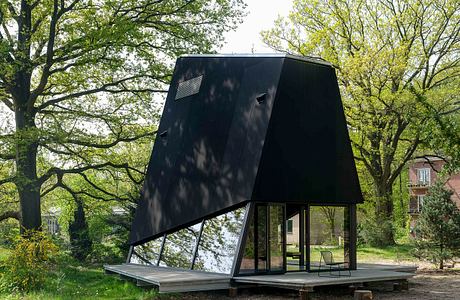 A striking black modern structure with glass walls and an angled roof, set in lush greenery.