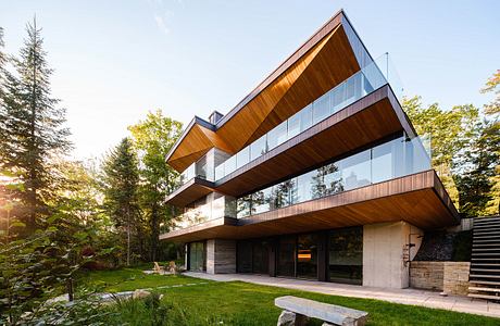 Striking modern design with wood, glass, and concrete elements, surrounded by lush greenery.