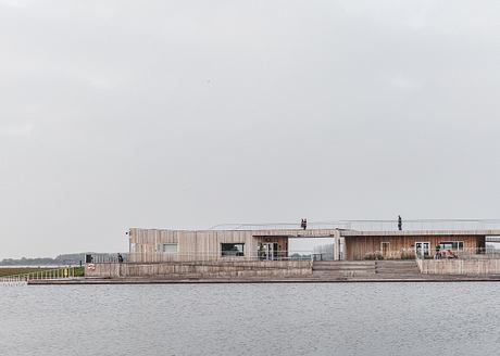 A modern, wooden-clad building with a large deck overlooking a body of water.