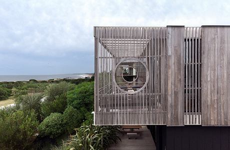 A wooden structure with a circular window and a lush, natural landscape in the foreground.