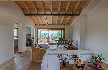 An open-concept living space with exposed wood beams, large windows, and a rustic aesthetic.