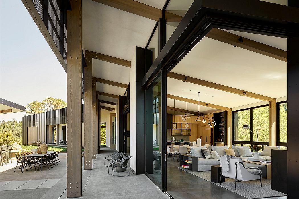 Contemporary open-plan living area with exposed wood beams, large windows, and outdoor dining.