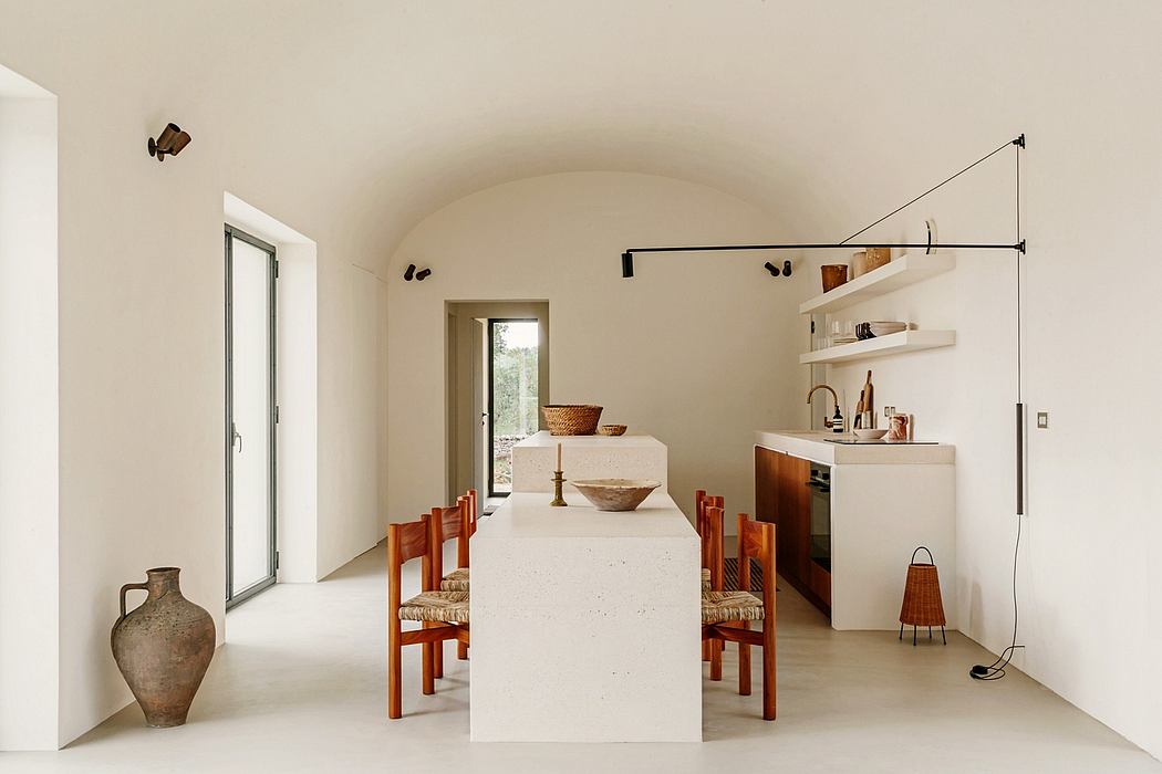 Minimalist dining area with white arched ceiling, wooden furnishings, and wall shelves.