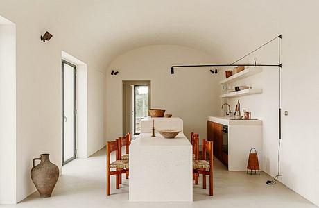 Minimalist dining area with white arched ceiling, wooden furnishings, and wall shelves.