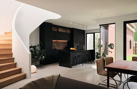 A modern, minimalist kitchen with black cabinetry, wood accents, and a curved staircase.