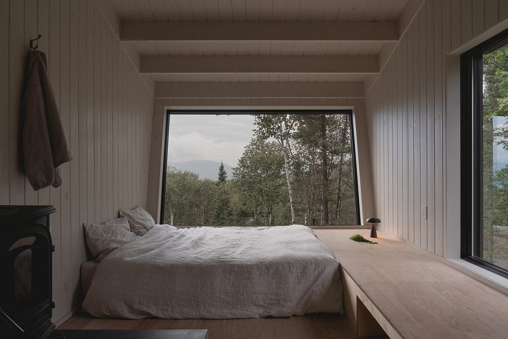 Cozy wood-paneled bedroom with large window framing scenic forest view.