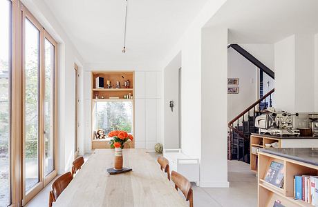 Bright, minimalist dining room with wooden table, shelves, and a view of the outdoors.