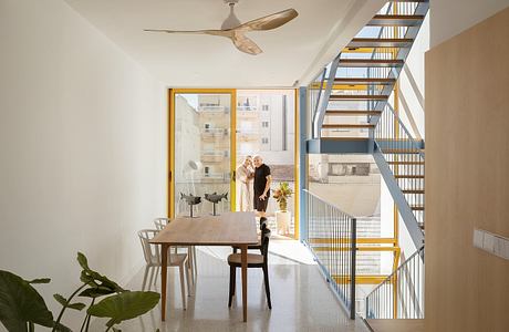 Modern open-concept interior with wooden table, metal stairs, and balcony view.