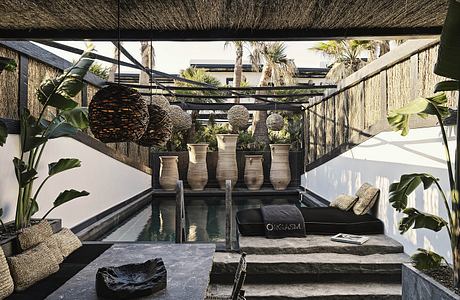 Lush tropical outdoor lounge with thatched roof, water feature, and modern decor.