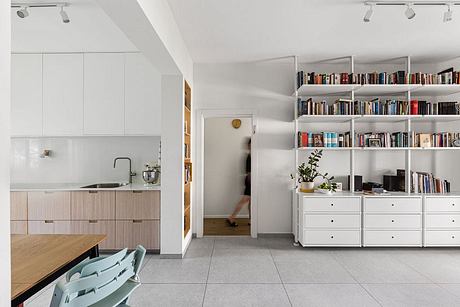 Modern open-plan kitchen and living area with built-in bookshelves, light wood and white tones.