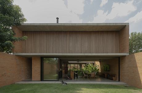 A modern brick and wood house with a large covered patio and lush greenery.