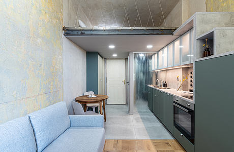 Modern kitchen with gray cabinets, wooden table, and blue sofa in compact space.