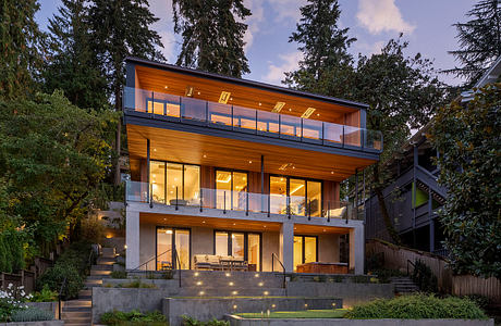 A modern, multi-story home with wooden siding, large windows, and a spacious balcony.