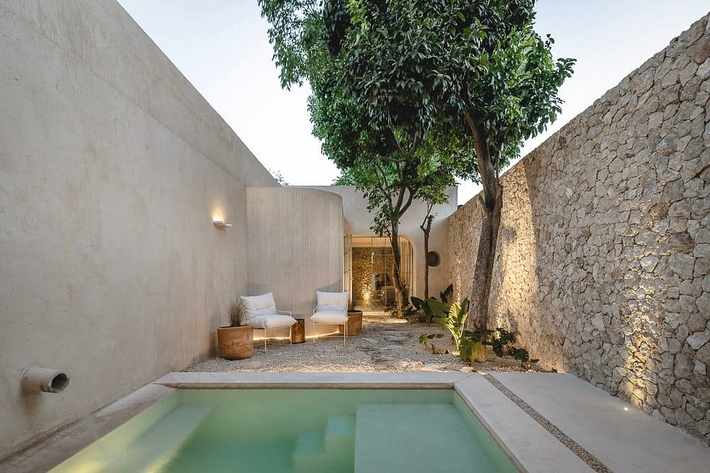 Warm, minimalist patio with small pool, stone walls, and lush tree centerpiece.