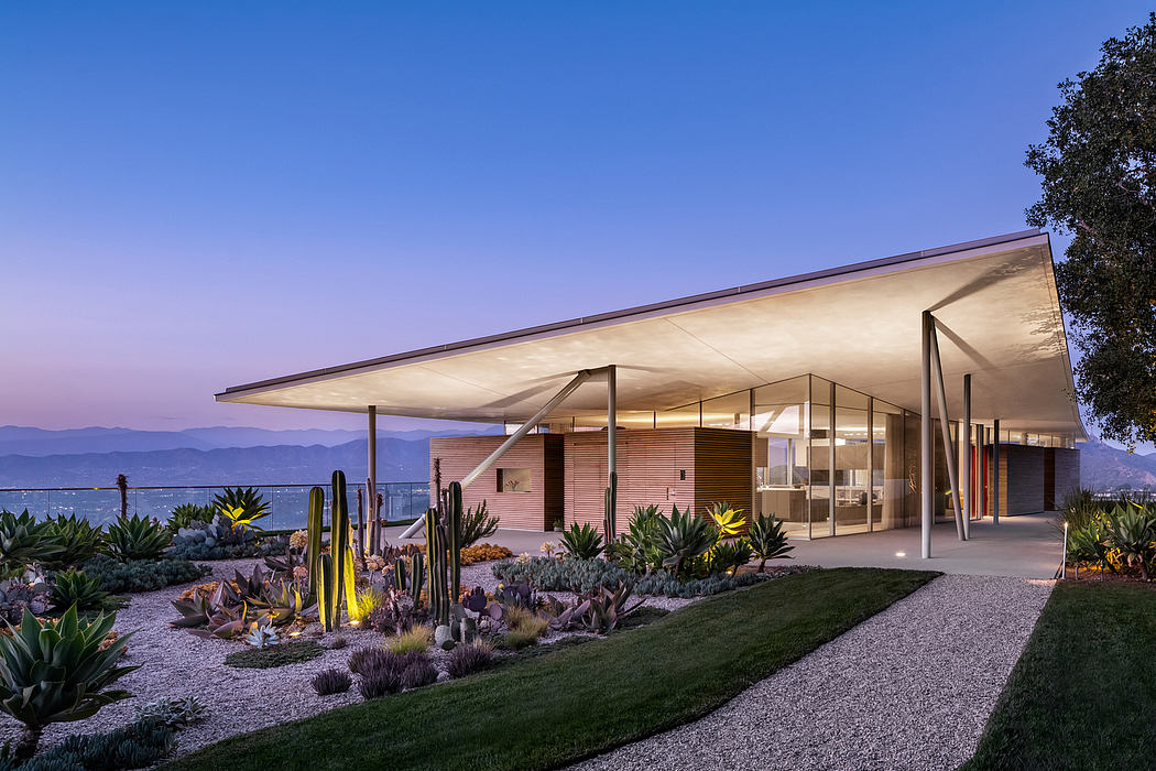 Modern desert residence with sleek roofline, glass walls, and lush, sculpted landscaping.