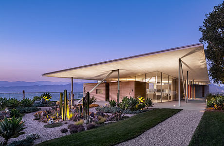 Modern desert residence with sleek roofline, glass walls, and lush, sculpted landscaping.