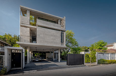 A modern, multi-story concrete building with balconies, large windows, and a car garage.
