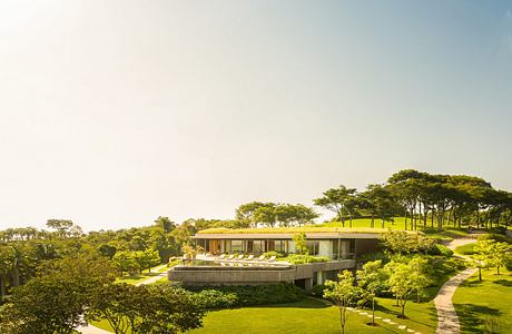 Modern single-story building nestled in lush green landscape with winding pathways.