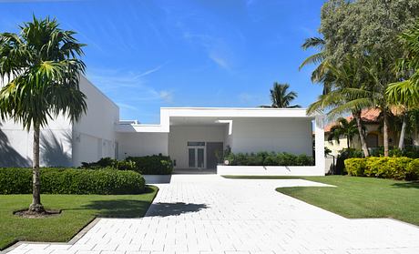 Striking modern architecture with clean lines, lush tropical landscaping, and paved entryway.