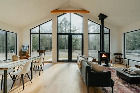 Cozy cabin with large windows, wood stove, and minimalist modern furnishings.