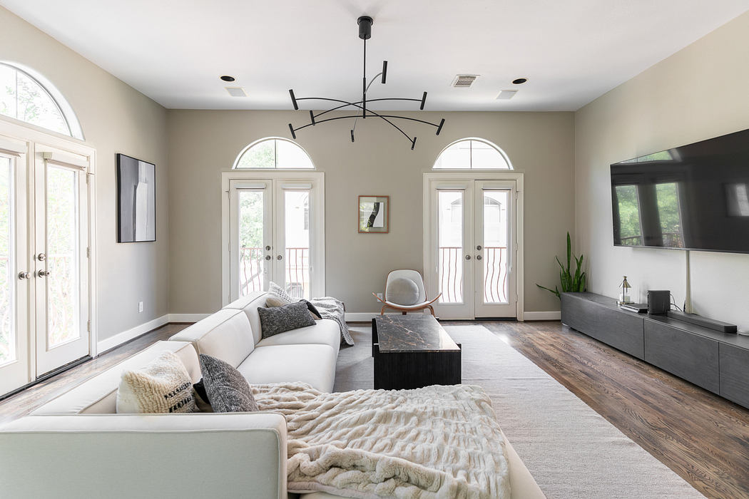 Spacious living room with arched windows, modern light fixture, and hardwood floors.