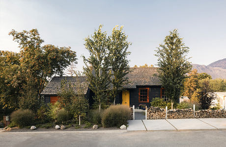 Cozy log cabin nestled among autumn trees, with a yellow door and stone pathway.