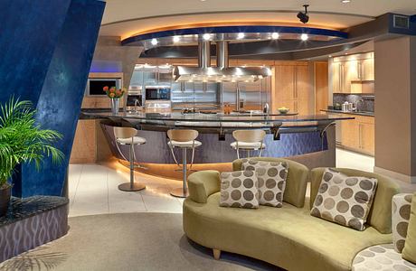 Modern kitchen with curved bar, chrome appliances, and plush sofa seating.