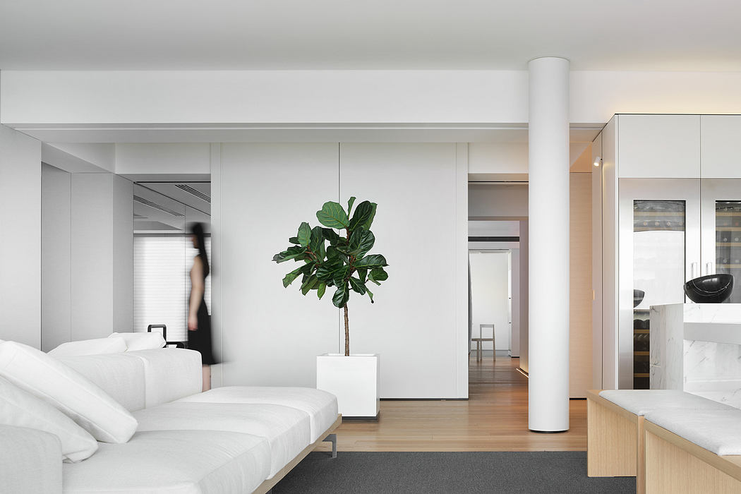 Spacious, minimalist bedroom with white furniture and a potted plant as the focal point.