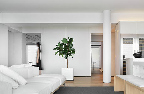 Spacious, minimalist bedroom with white furniture and a potted plant as the focal point.