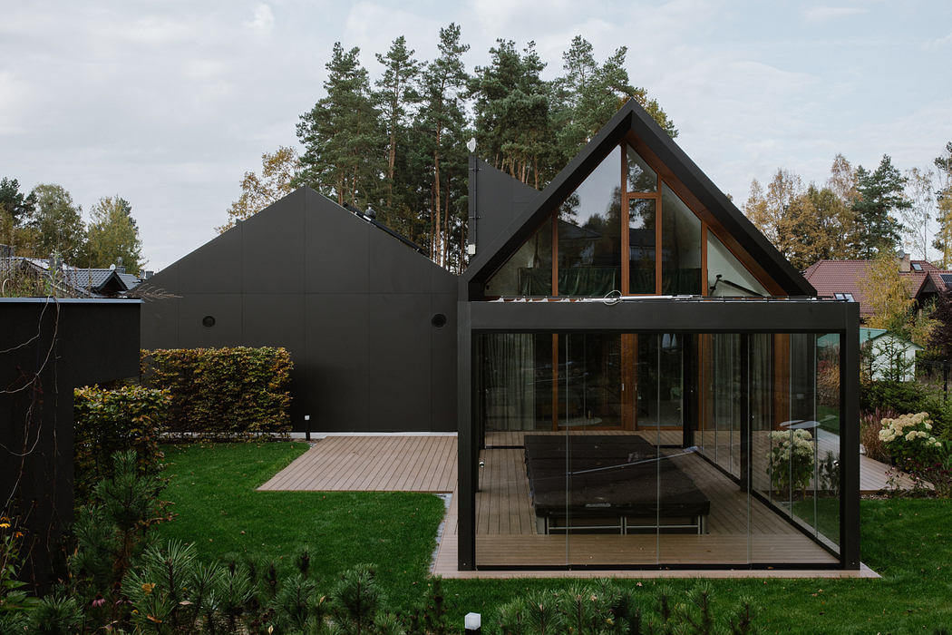 Modern geometric house with floor-to-ceiling windows, wooden deck, and lush landscaping.