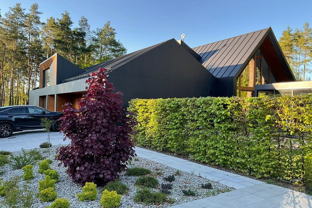 A modern, sleek black house with distinctive roofline and landscaped garden surround.