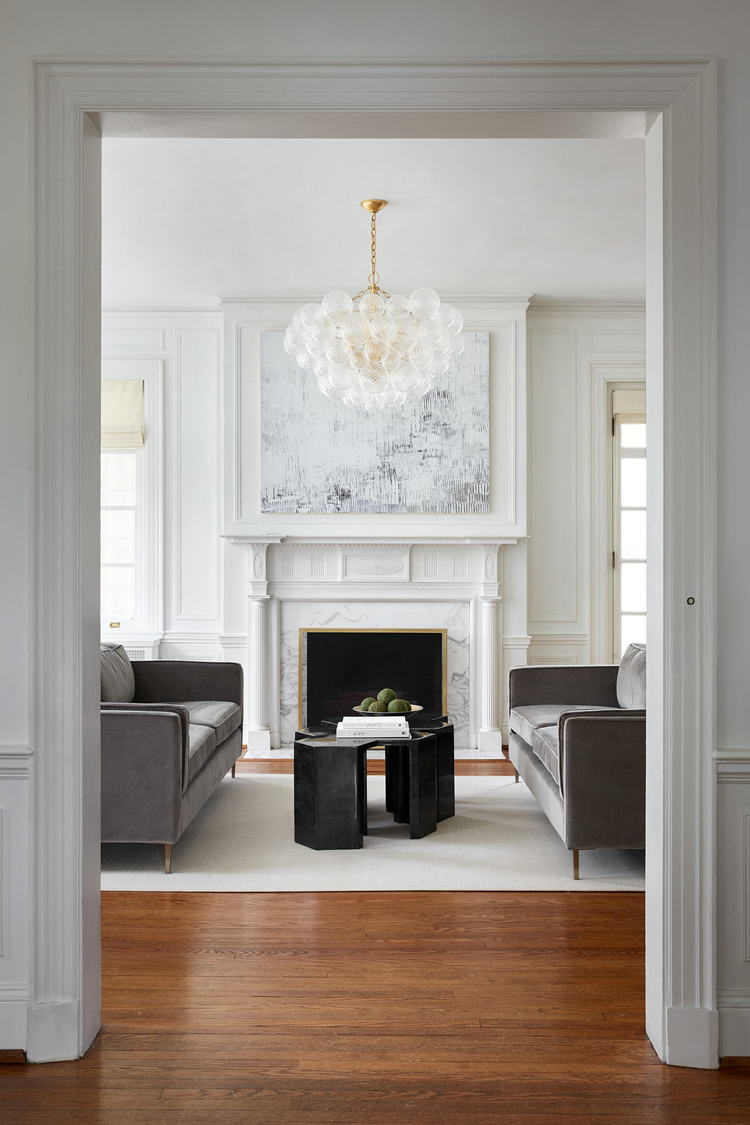 Elegant white room with ornate fireplace, modern furnishings, and a stunning chandelier.