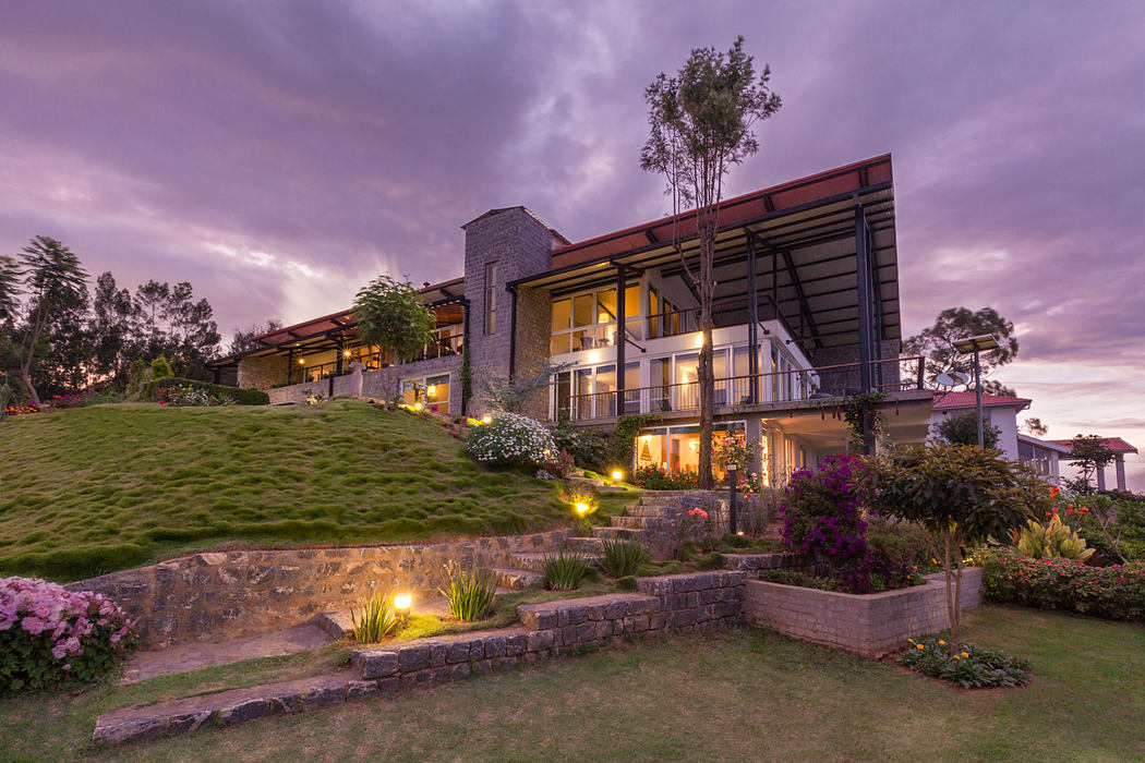 Stunning modern hillside home with stone facade, tiered landscaping, and illuminated accents.
