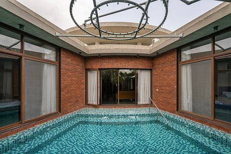 Striking indoor pool surrounded by brick walls and glass windows, featuring a unique overhead lighting fixture.