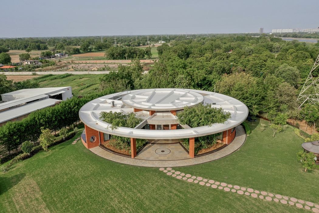 Circular structure with brick walls and a distinctive white roof design surrounded by lush greenery.