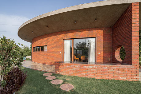 Curved brick facade with large windows and paved walkway leading to grassy yard.