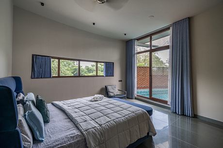 Spacious bedroom with large windows, modern furnishings, and access to an outdoor pool.